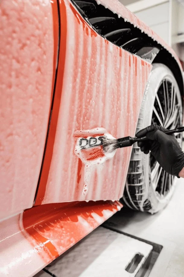 Hand brushing foam off the wing of an orange supercar during a detailing wash