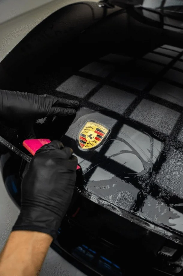 Squeegee smoothing paint protection film over the bonnet of a black Porsche
