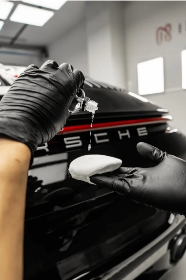 Keramikversiegelung wird mit einem Schaumapplikator auf das Heck eines schwarzen Porsche aufgetragen